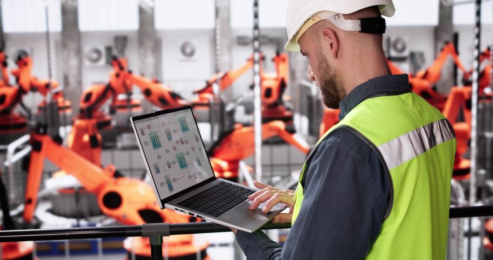 A man is using a laptop computer in a factory.