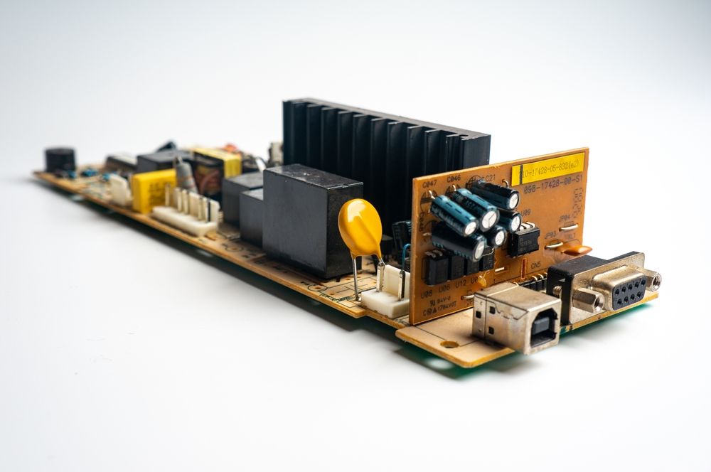 Circuit board with black heat sink, yellow capacitor, and USB ports on a white background
