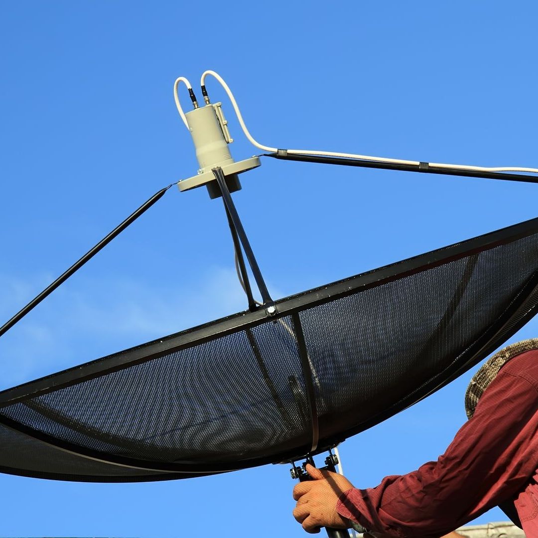 A man in a red shirt is working on a satellite dish