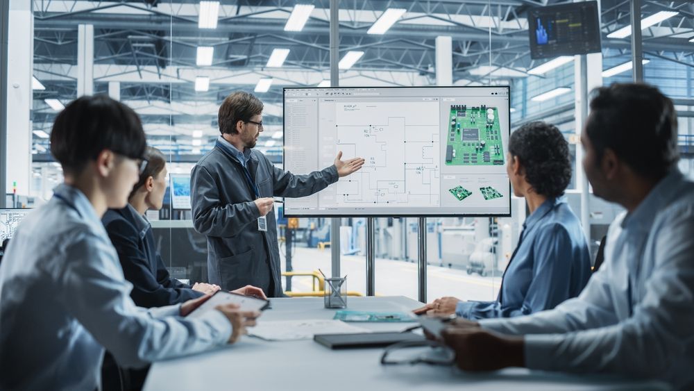 Team meeting in a modern office, with a presenter pointing at a whiteboard display with charts.