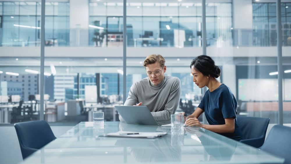 Two people reviewing laptop in modern office; man pointing, woman looking on.