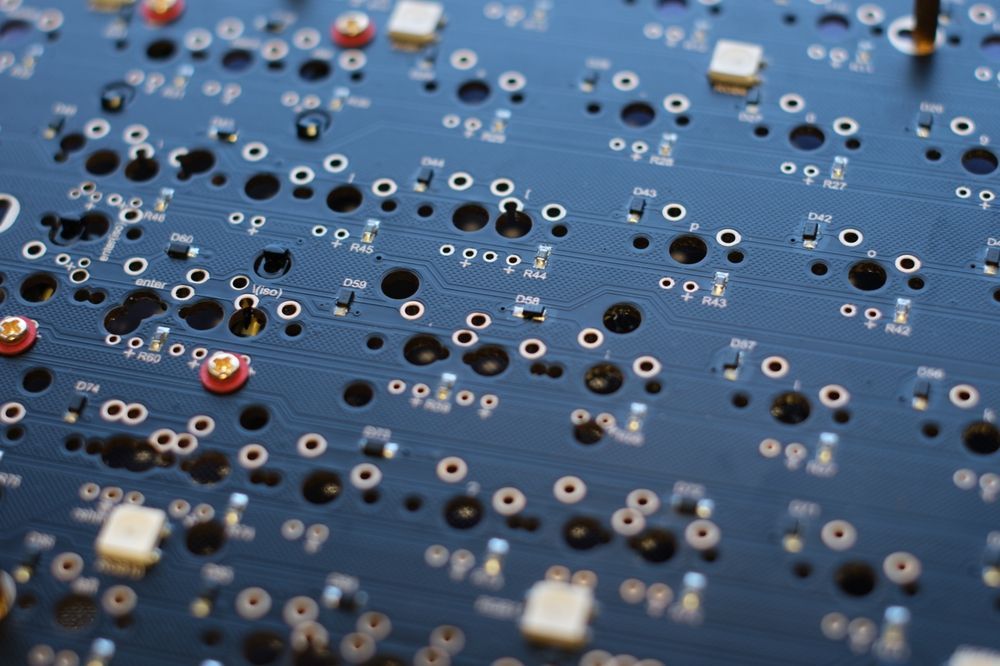 Close-up view of a dark blue printed circuit board with many holes, and a few mounted components.