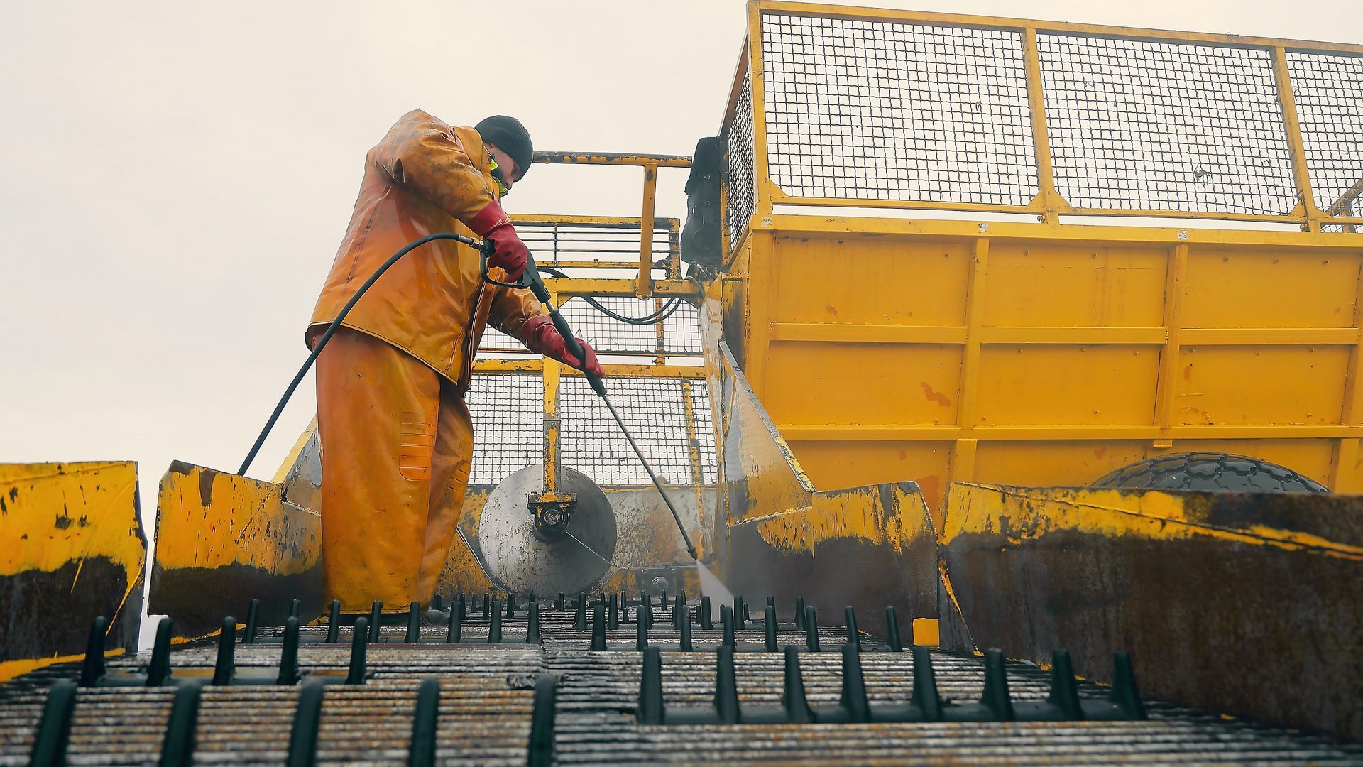 A man is cleaning a yellow truck with a high pressure washer.