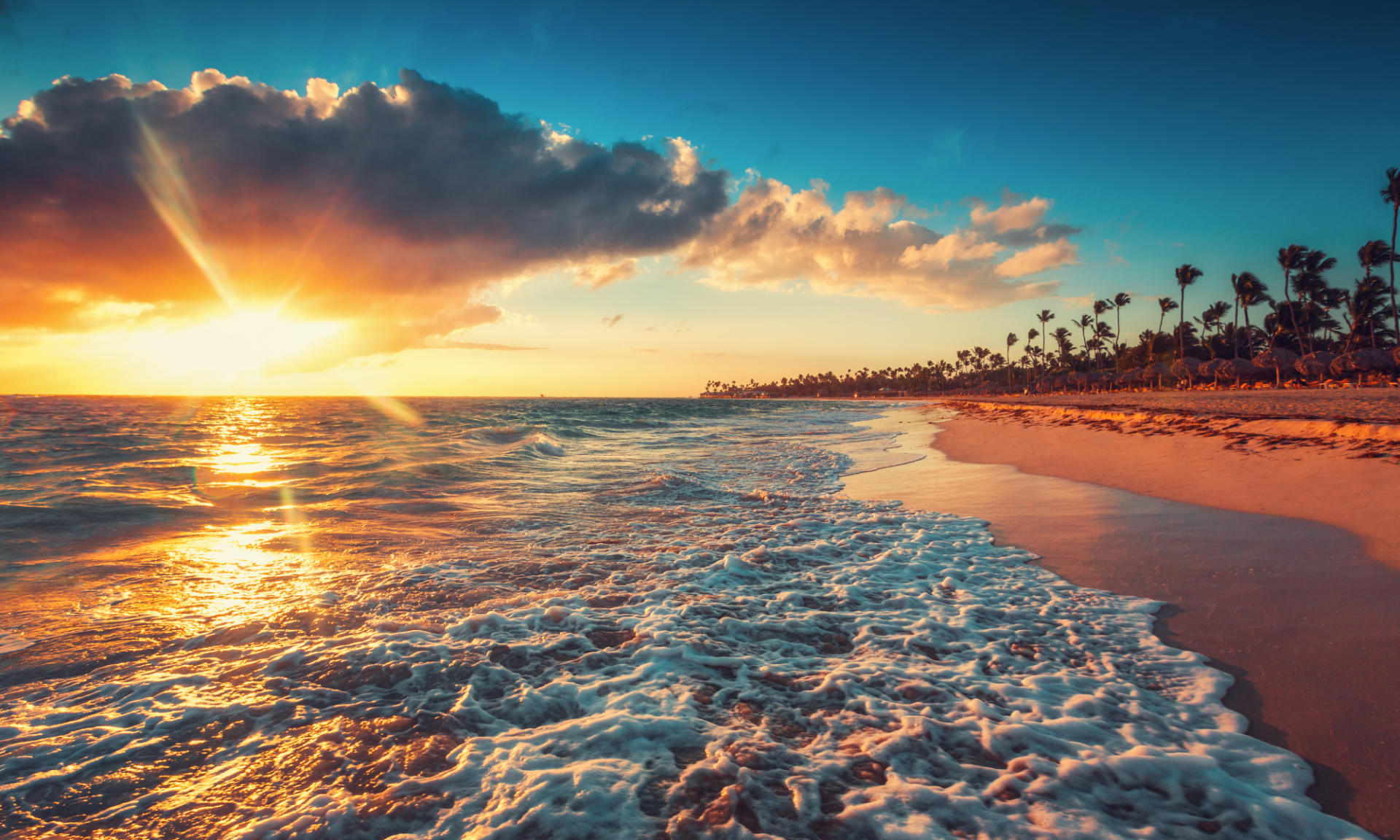 The sun is setting over the ocean on a tropical beach.
