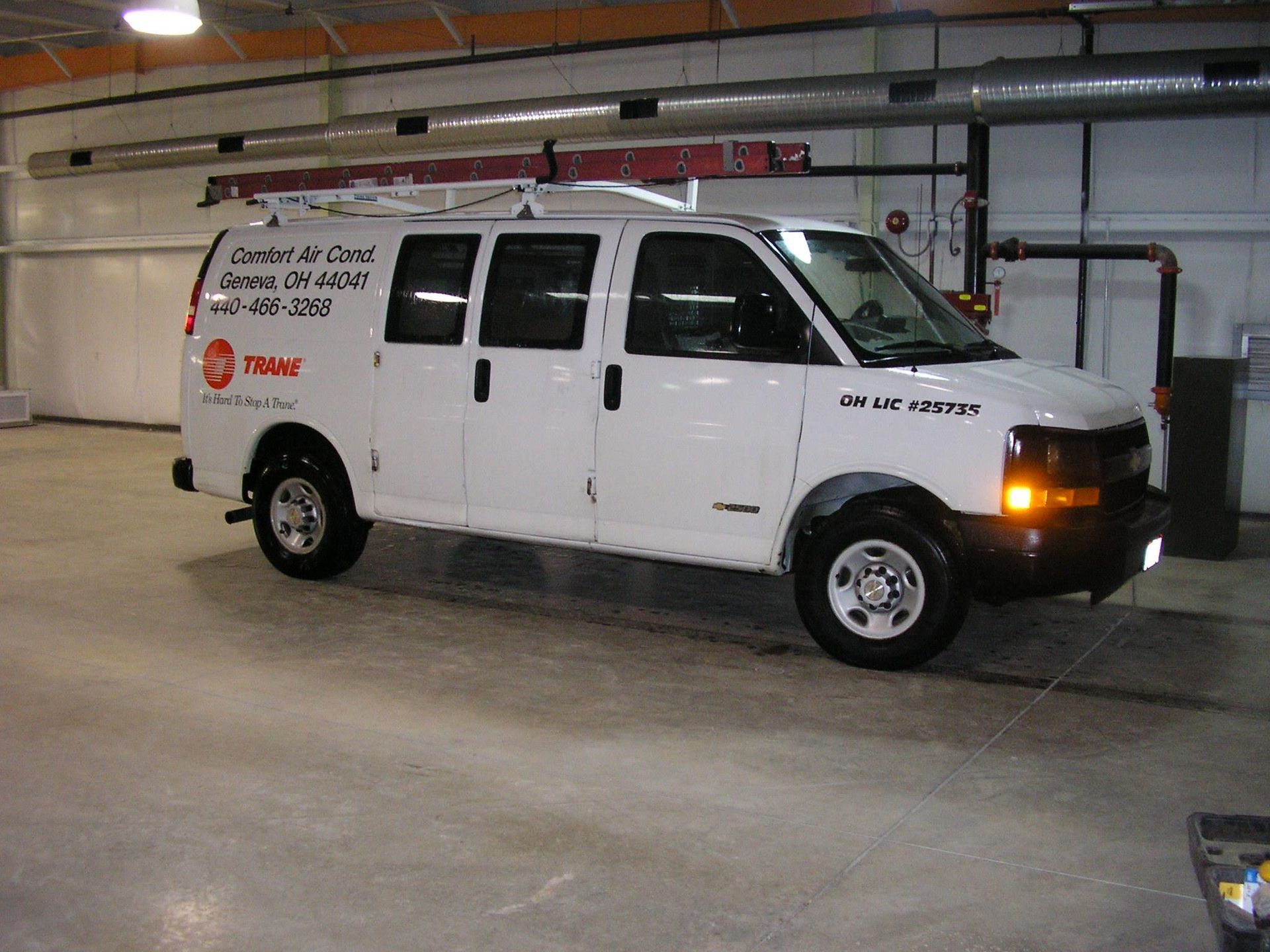 A white van is parked in a garage with a phone number on the side