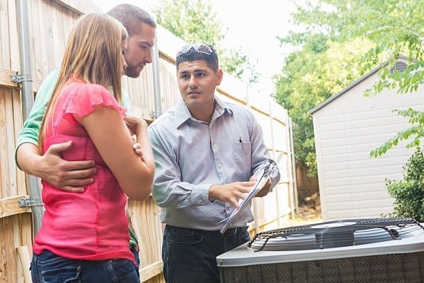 A man is talking to a woman and a man in front of an air conditioner.