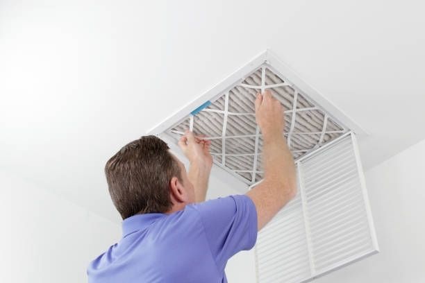 A man is cleaning an air vent on the ceiling.