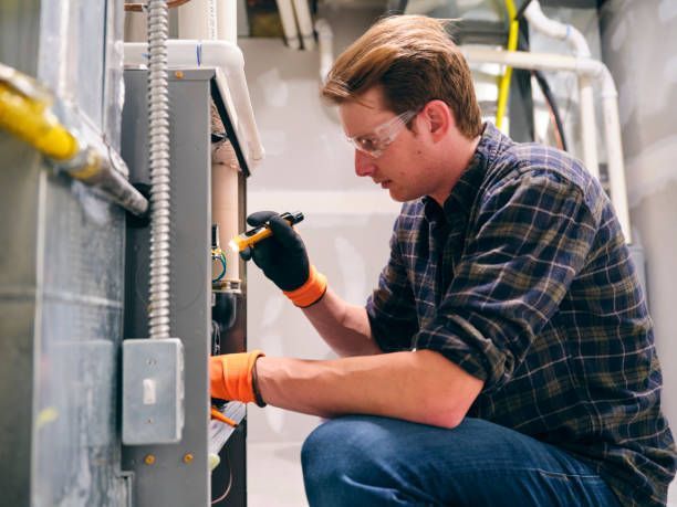 A man is kneeling down and working on an air conditioner.