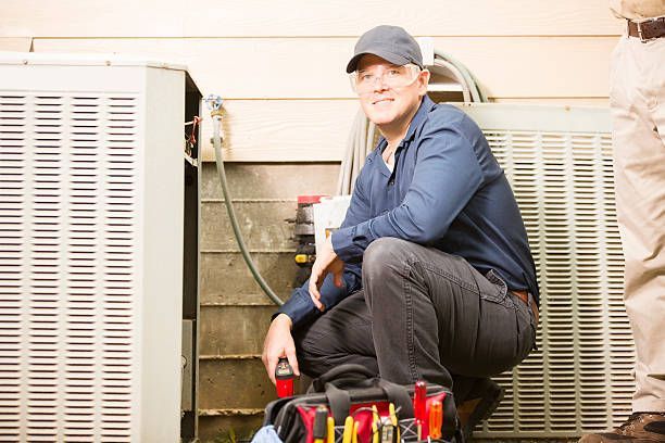A man is kneeling down next to an air conditioner.