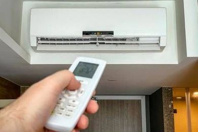 A person is holding a remote control in front of an air conditioner.