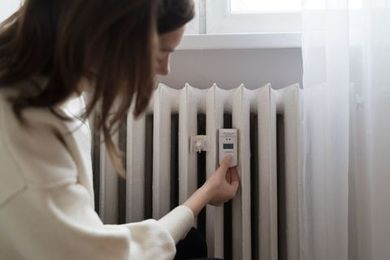 A woman is adjusting a thermostat on a radiator.