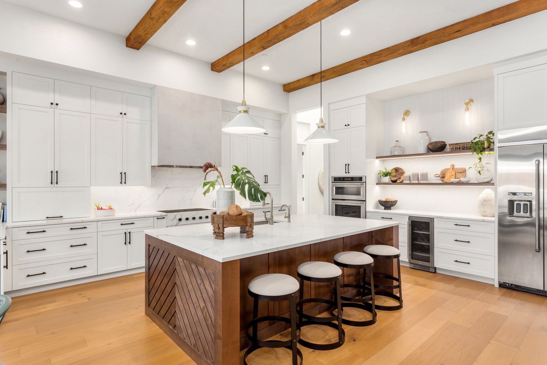 A kitchen with white cabinets , wooden floors , stools and a large island.