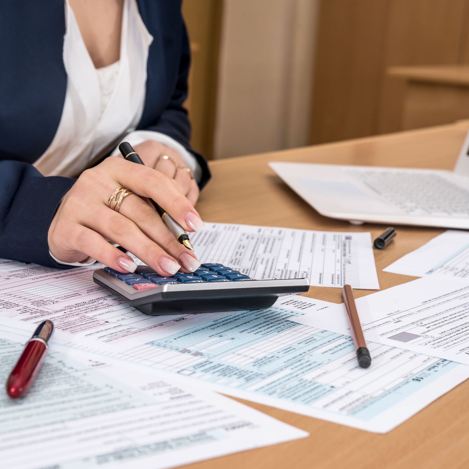 Person using a calculator surrounded by tax forms and a laptop.