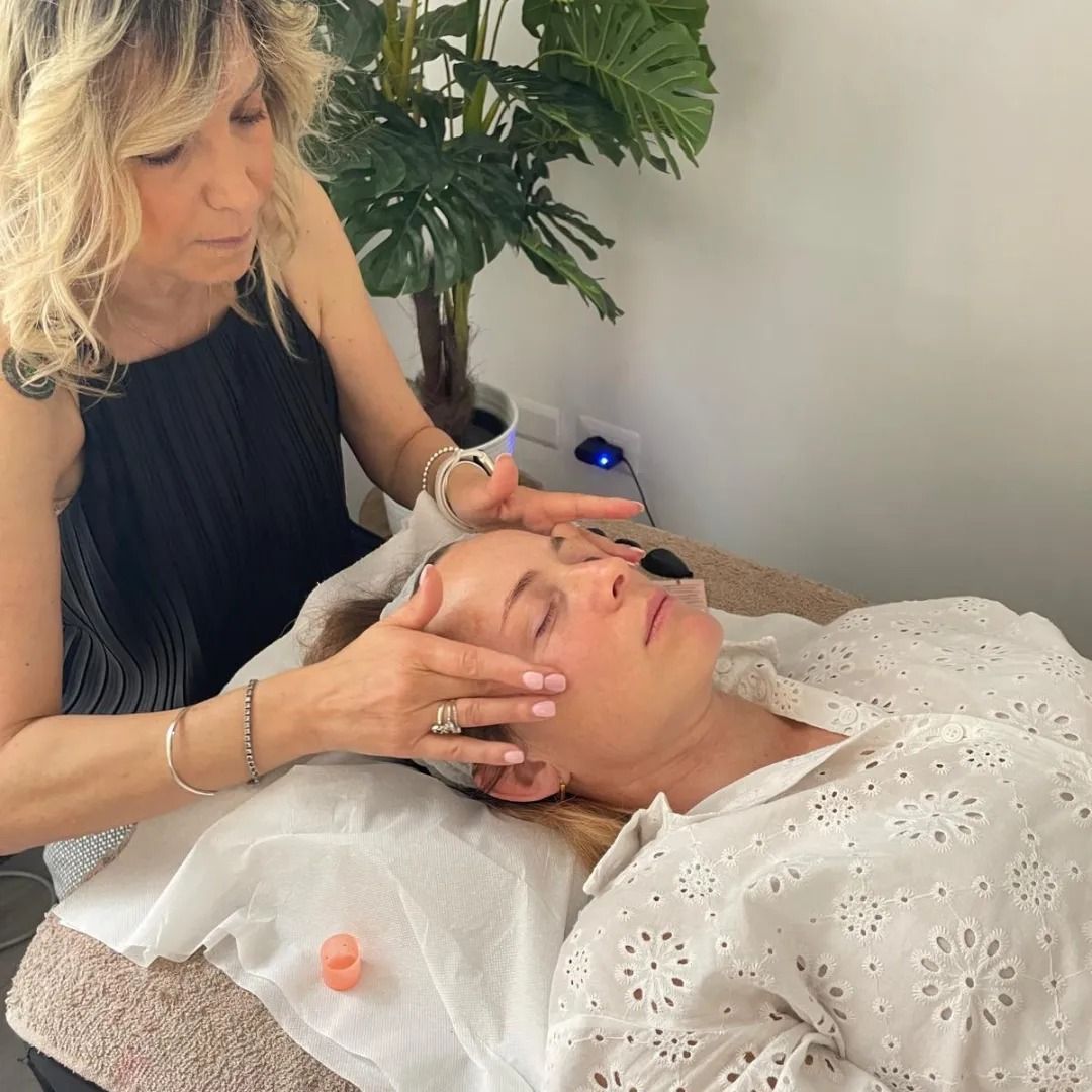 Una donna riceve un trattamento viso mentre un'altra donna le massaggia il viso in un ambiente simile a una spa.