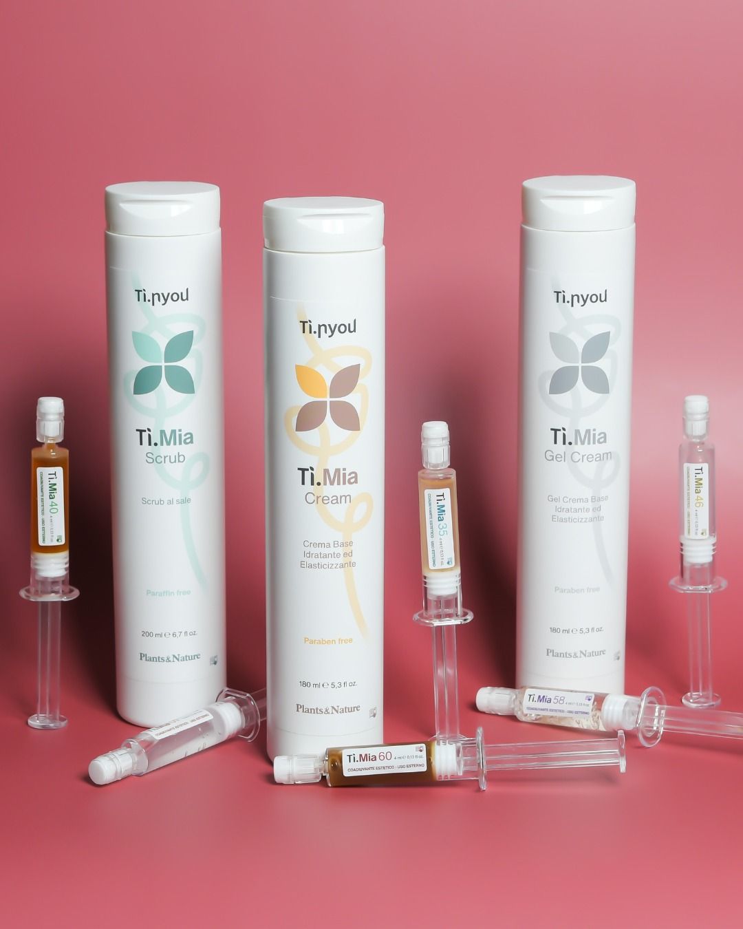 Espositore per prodotti cosmetici con tre alte bottiglie bianche e piccole siringhe, su uno sfondo rosa.