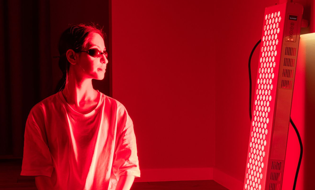 Una donna con gli occhiali è in piedi sotto una luce rossa, di fronte al pannello luminoso rosso.