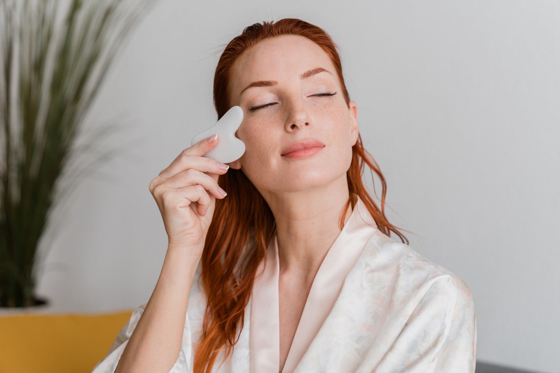 Donna che usa uno strumento sulla guancia. Indossa una tunica e ha gli occhi chiusi.