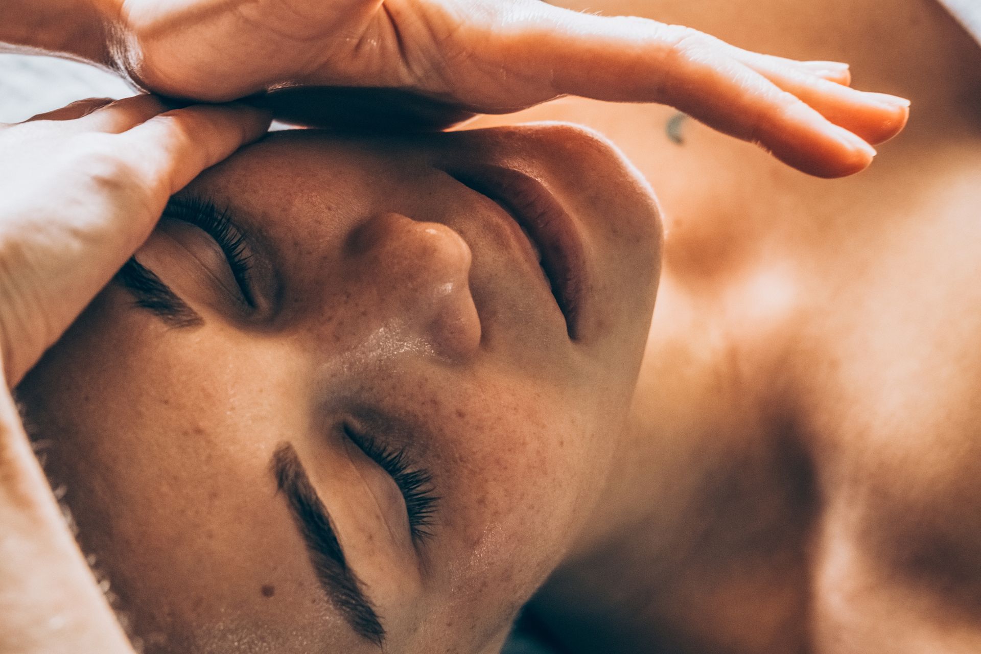 Persona che riceve un massaggio facciale con gli occhi chiusi e le mani sopra la fronte.