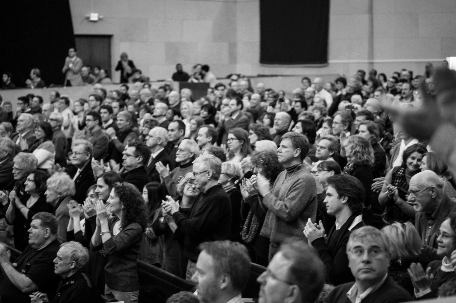 A large group of people are sitting in a theater applauding.