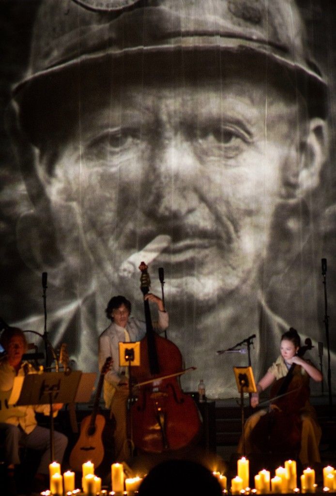 A group of musicians are playing in front of a large projection of a man 's face