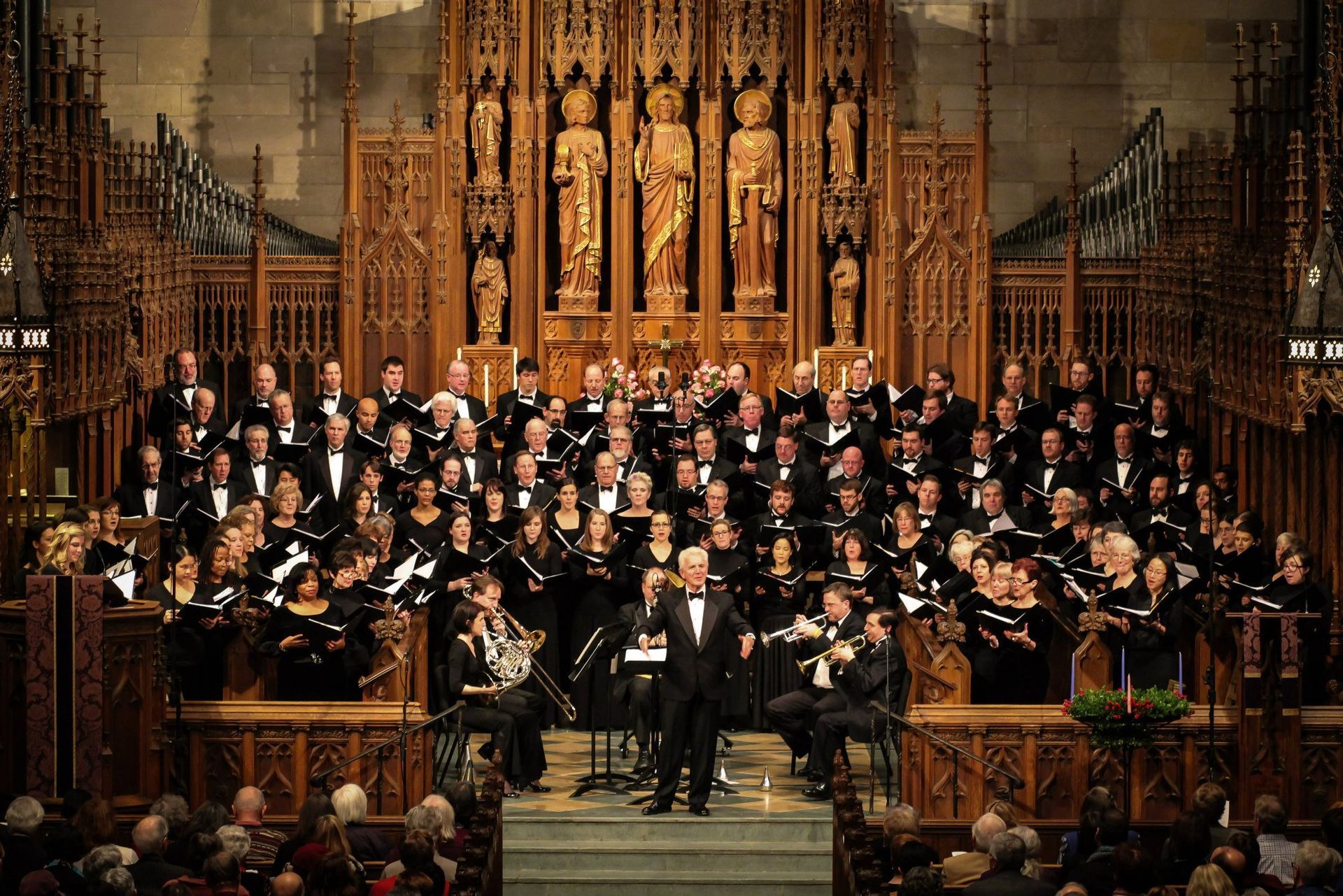 Choir and orchestra performing on a stage in a gothic church; audience in foreground.