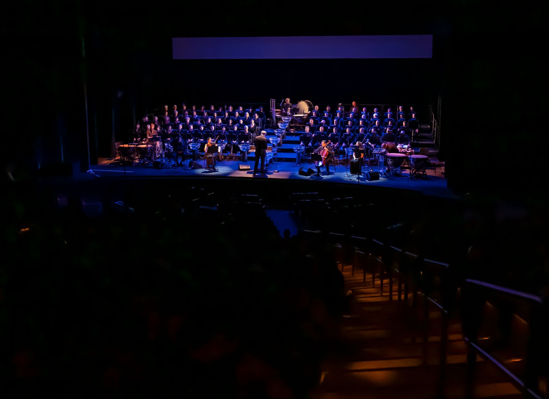 A choir is performing on a stage in a dark auditorium