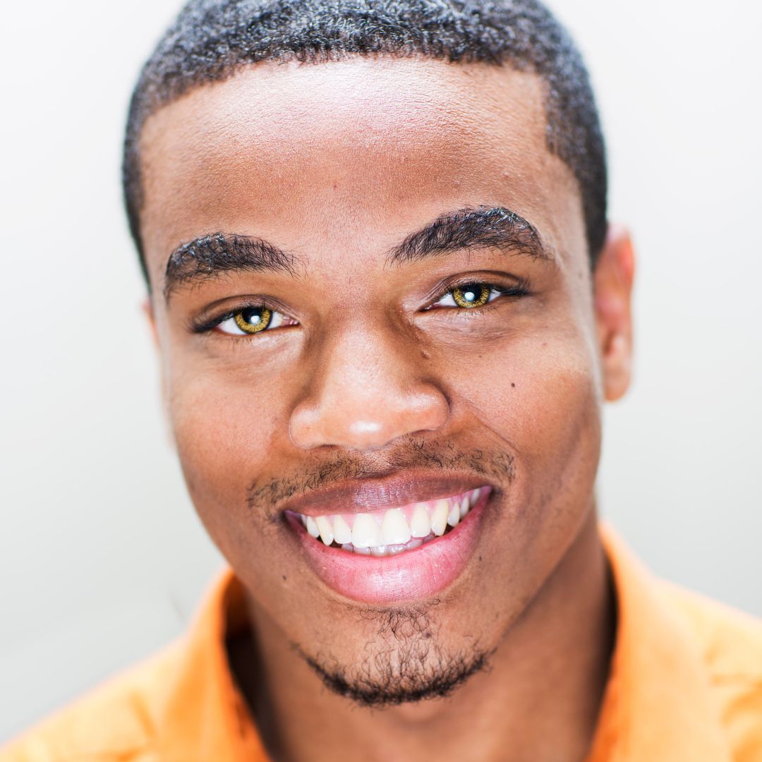 A young man wearing an orange shirt is smiling for the camera.