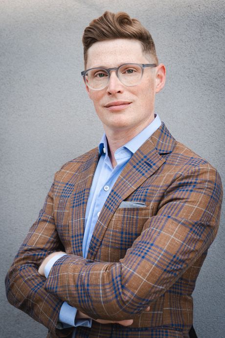 A man wearing glasses and a purple pocket square is smiling.