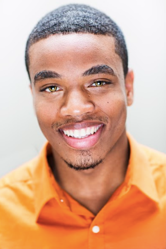 A young man wearing an orange shirt is smiling for the camera.
