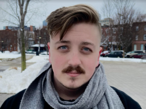 A man with a mustache wearing a scarf looks at the camera