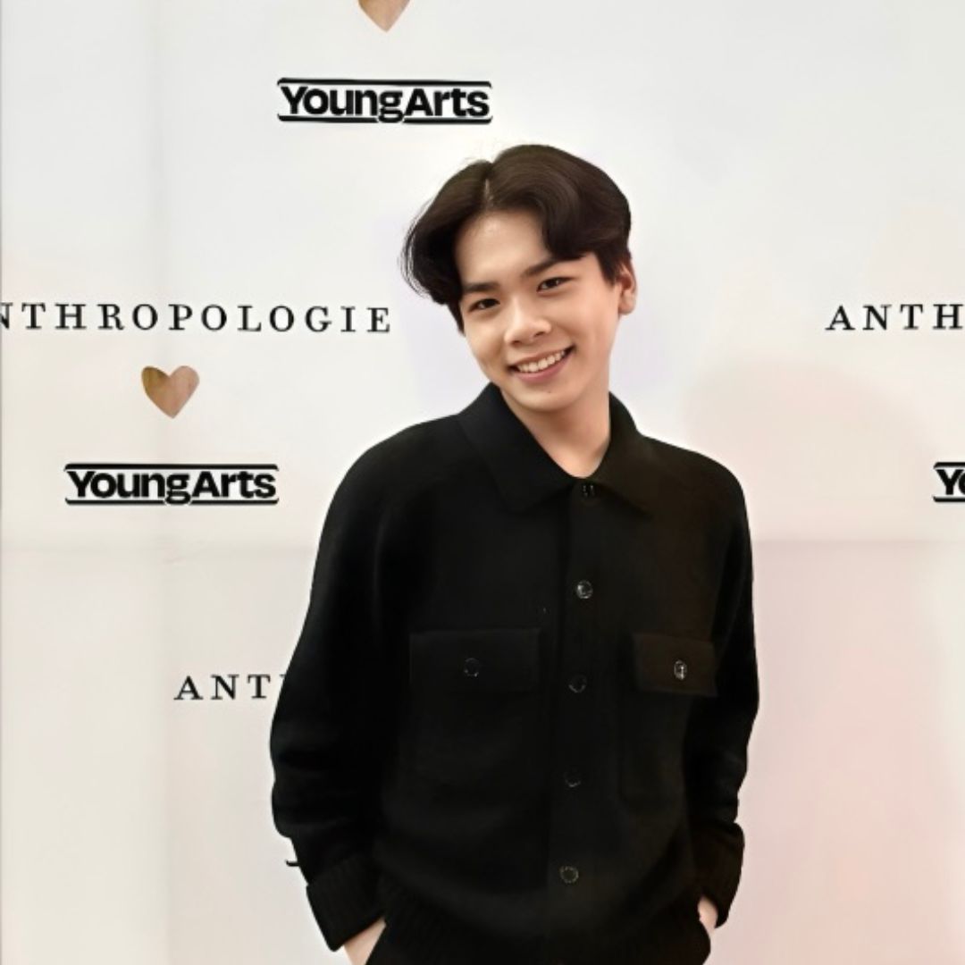 Young Asian man smiles, wearing a black button-down shirt, standing in front of a YoungArts and Anthropologie backdrop.