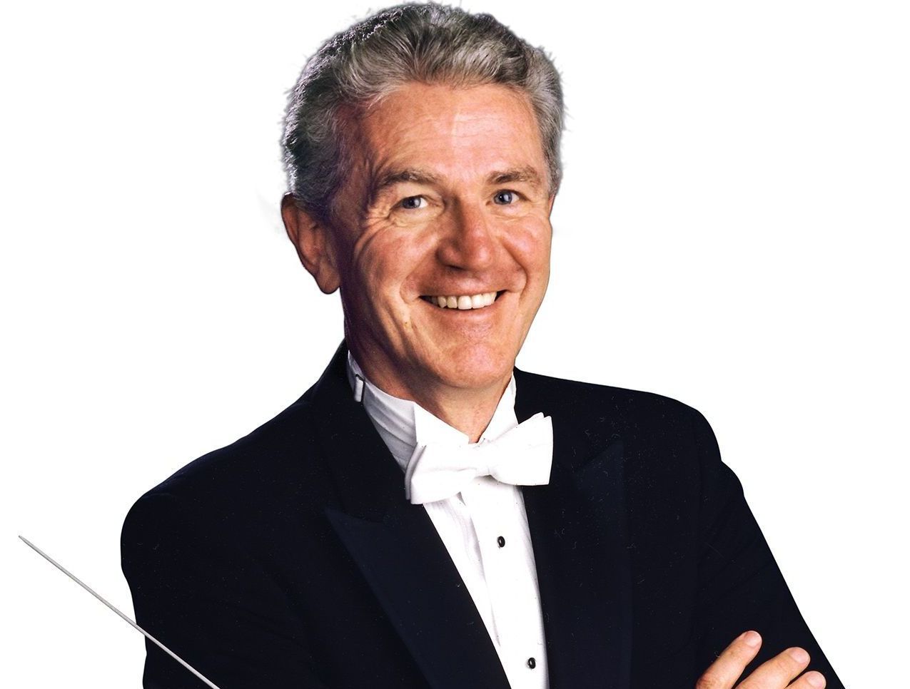 A man in a tuxedo and bow tie is smiling with his arms crossed