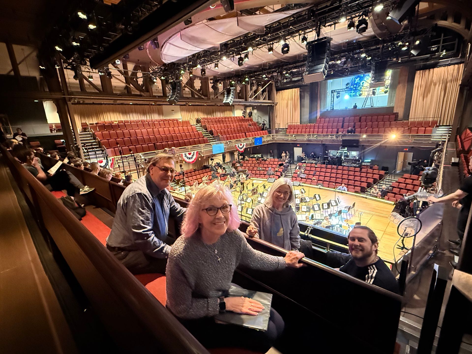 Four people smiling in an elevated theater box, overlooking a red-seated auditorium.