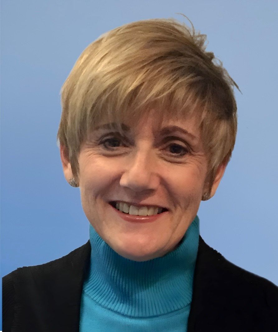 A woman wearing a blue turtleneck and a black jacket smiles for the camera