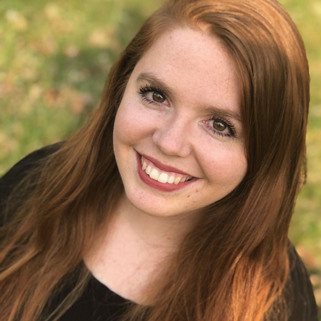 A woman with long red hair and freckles is smiling for the camera.