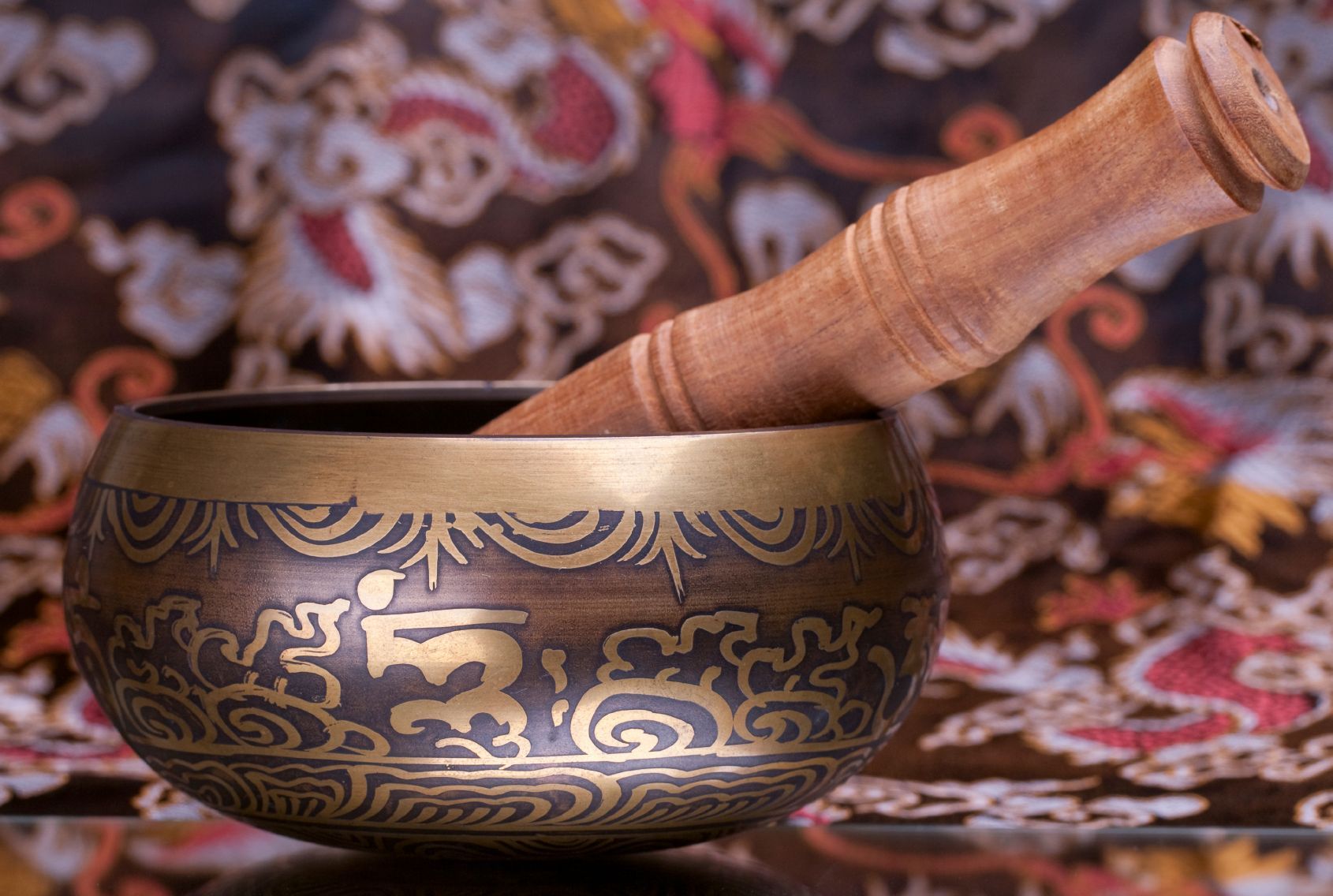 A brass bowl with a wooden stick in it is sitting on a table.