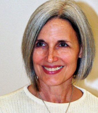 A woman with gray hair is smiling and wearing a white sweater.