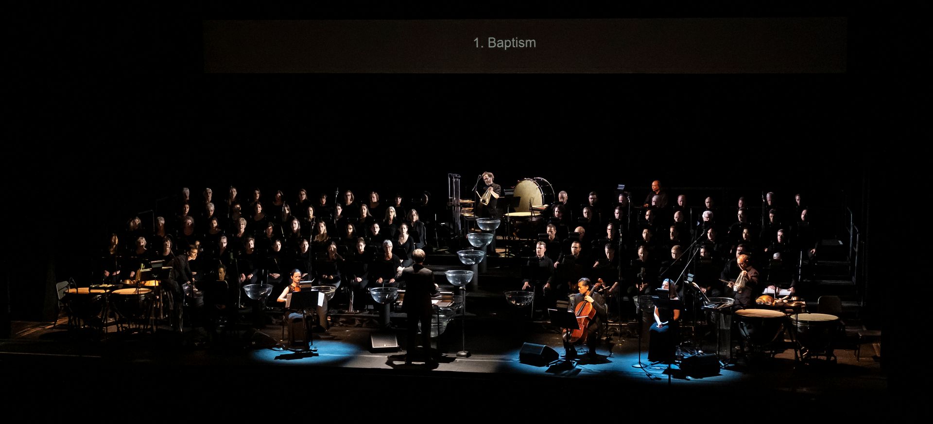A large orchestra is playing on a stage in a dark room.