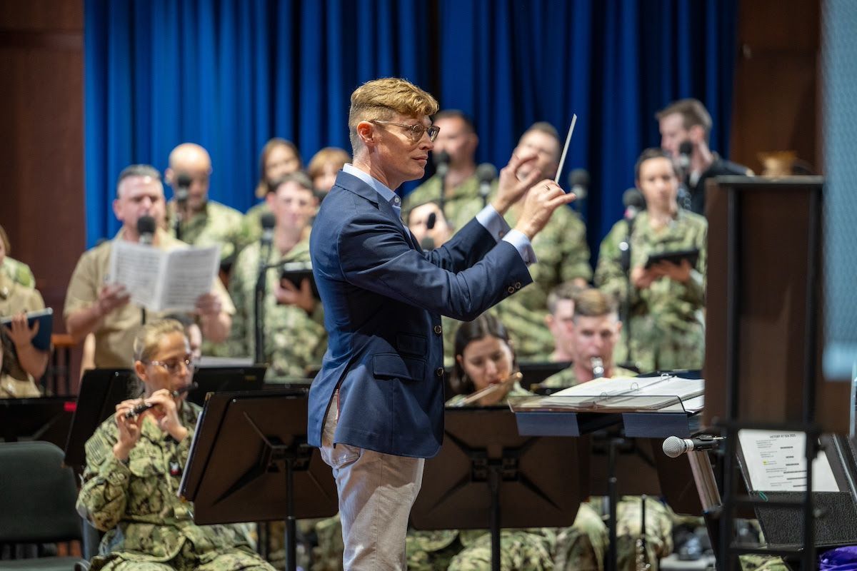 A conductor leads a military band and choir in a performance.