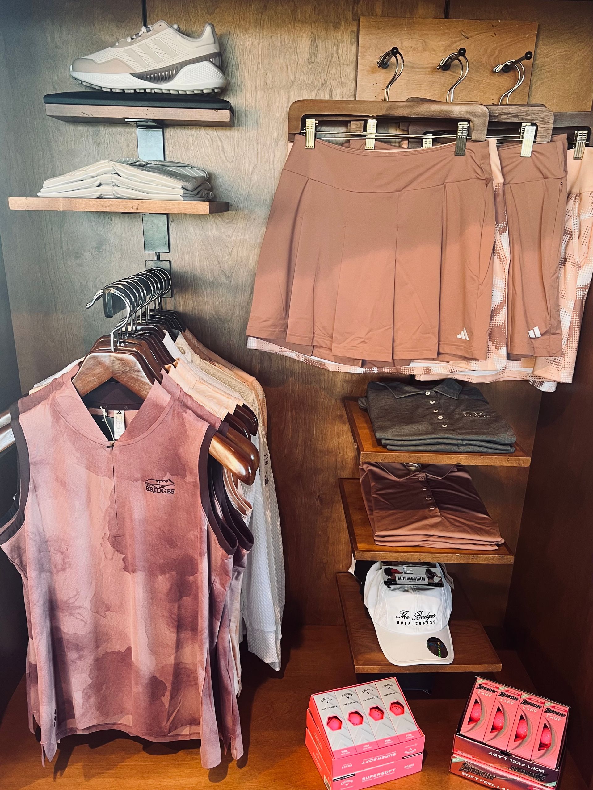 Clothing display with shirts, skirts, hats, shoes, and golf balls in brown and pink hues.