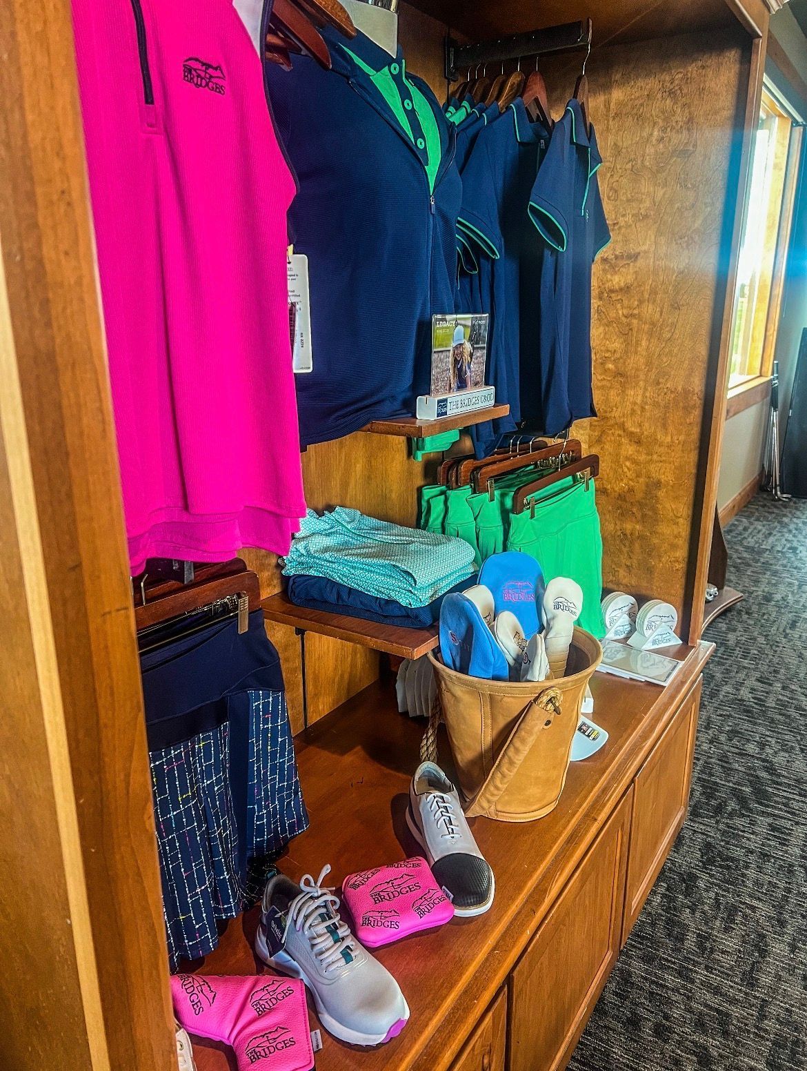 Clothing display in a wooden cabinet, featuring golf attire in shades of pink, blue, and green.