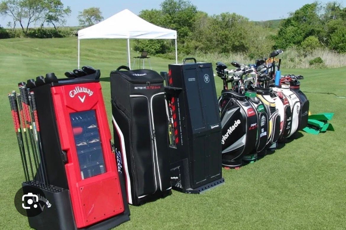 Golf bags and equipment on green grass with a white tent in the background.
