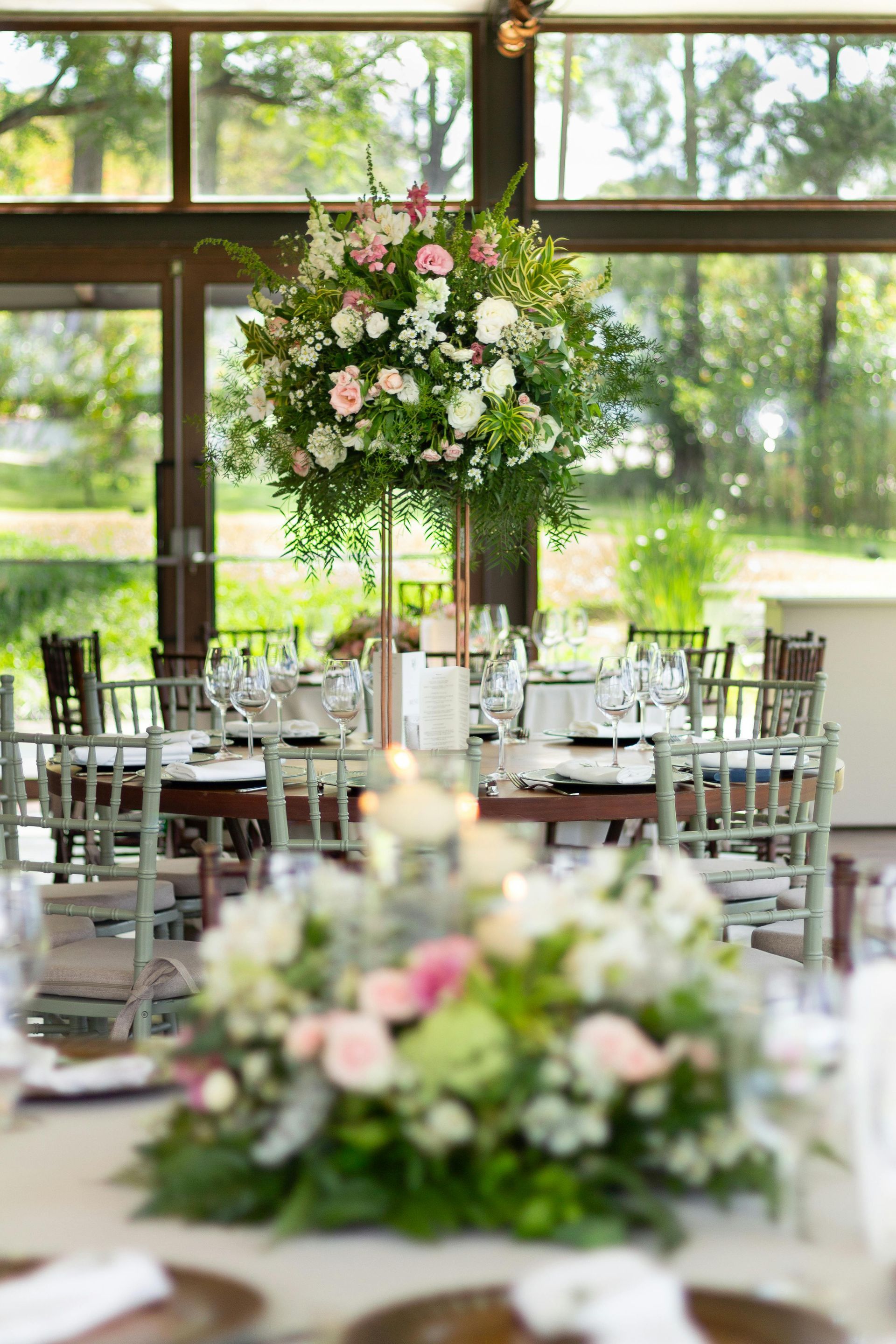 Elegant floral centerpieces on a round table, set for a formal event, with surrounding chairs and outdoor view.