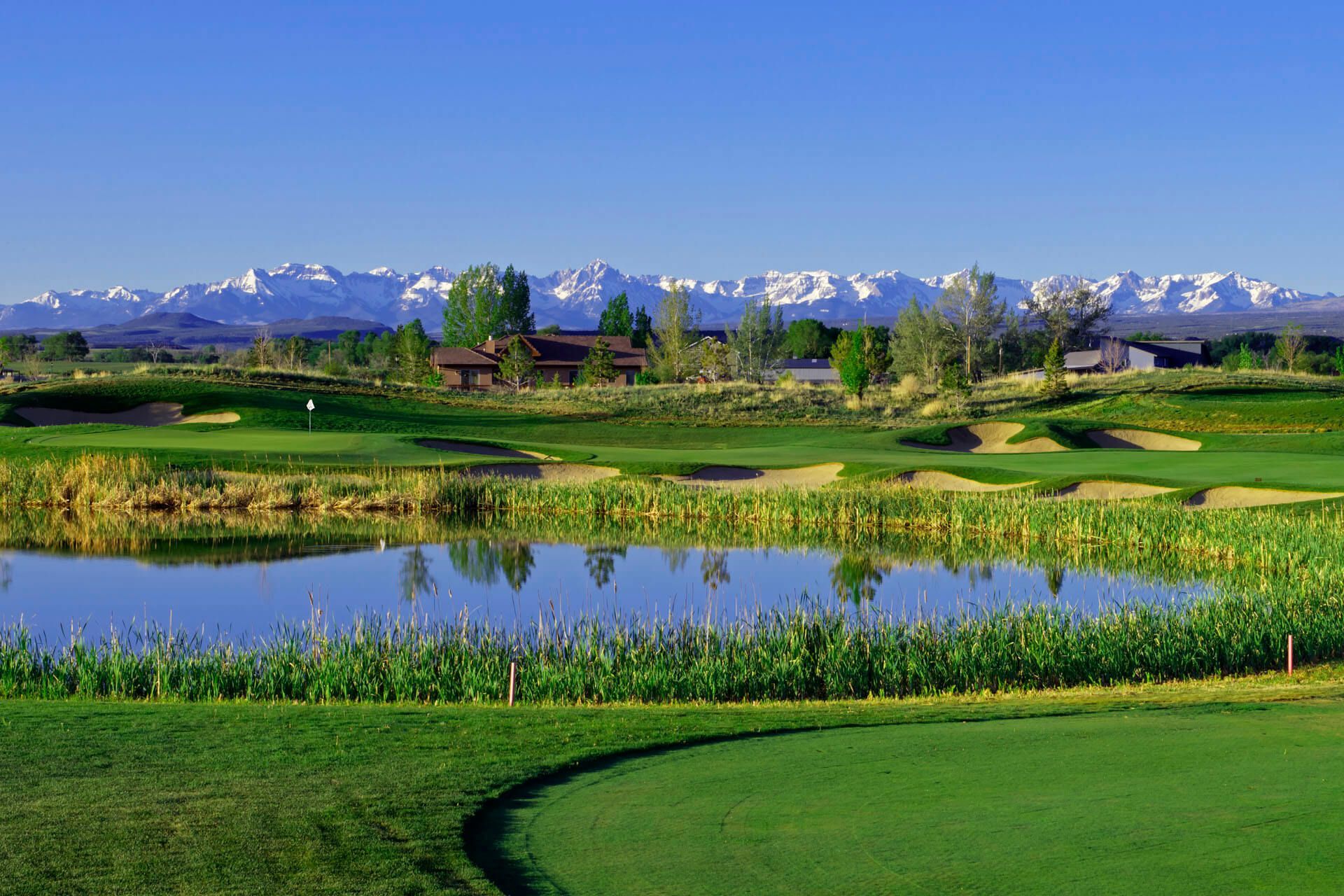 Golf course with a lake and mountains in the background under a blue sky.