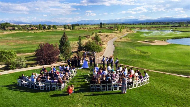 Wedding ceremony on a golf course with guests seated facing a couple standing near a small gathering of people.