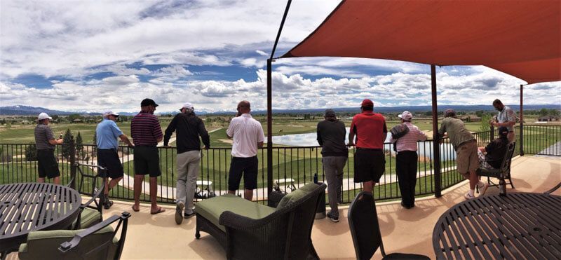 People overlooking a golf course from a patio with an orange canopy and cloudy sky.