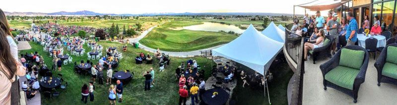 Large outdoor gathering on a green hill with tents and people; a golf course in the background.