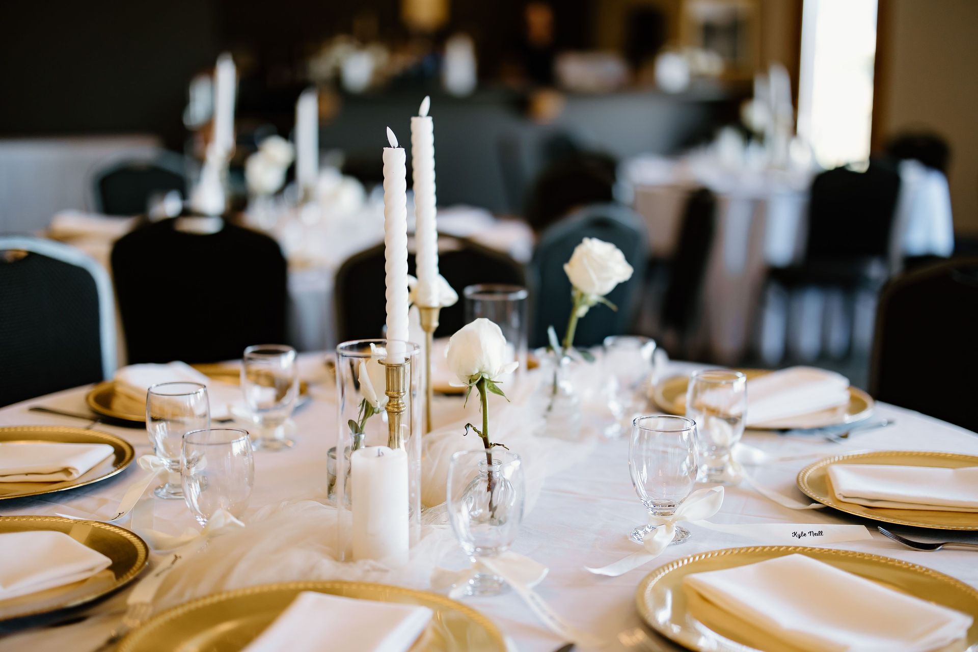 Wedding reception table setting with candles, roses, and gold-rimmed plates.