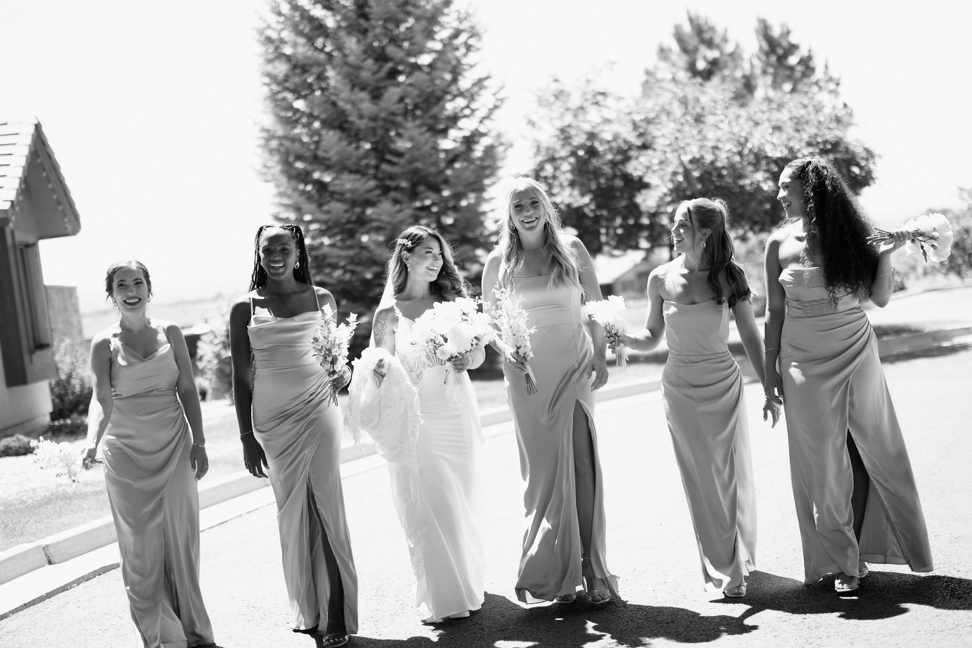 Bride with bridesmaids in gowns, walking on a street, laughing with joy.