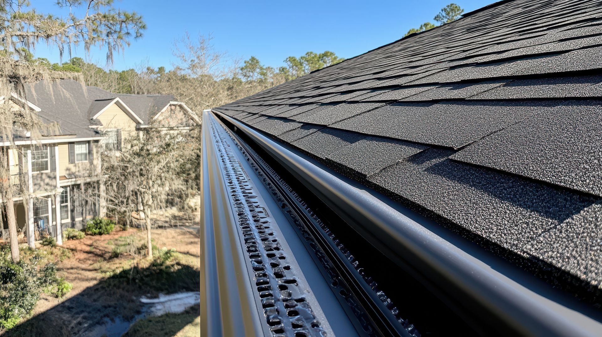 White rain gutters and downspouts on a building with a gray metal roof.